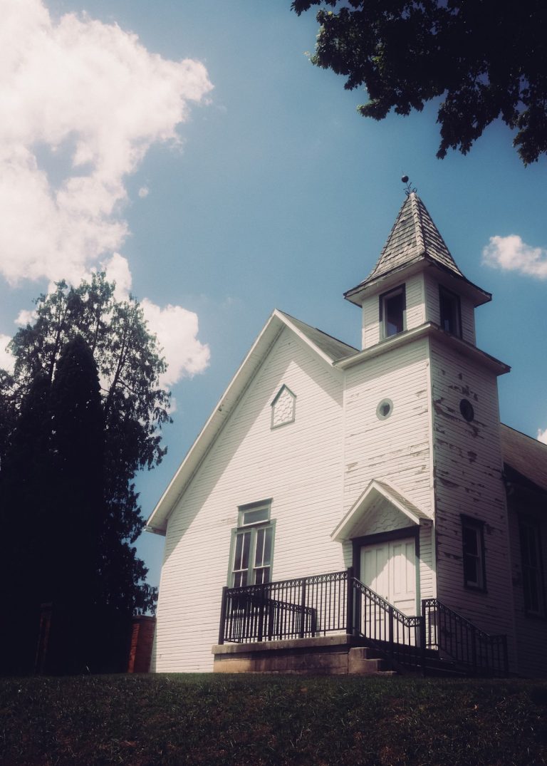 A weathered white church building against a bright blue sky